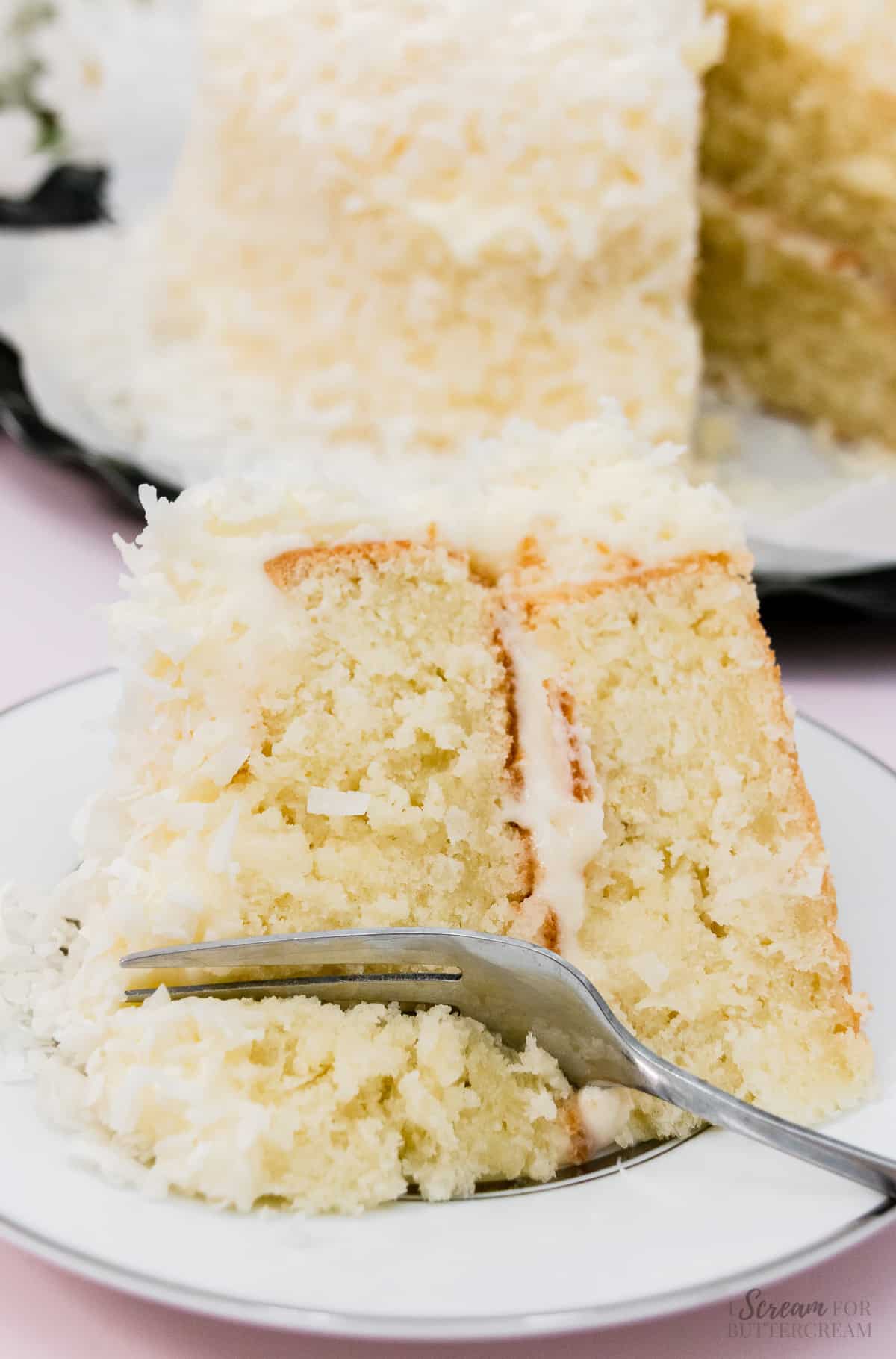 Slice of coconut cake with a fork on a plate.