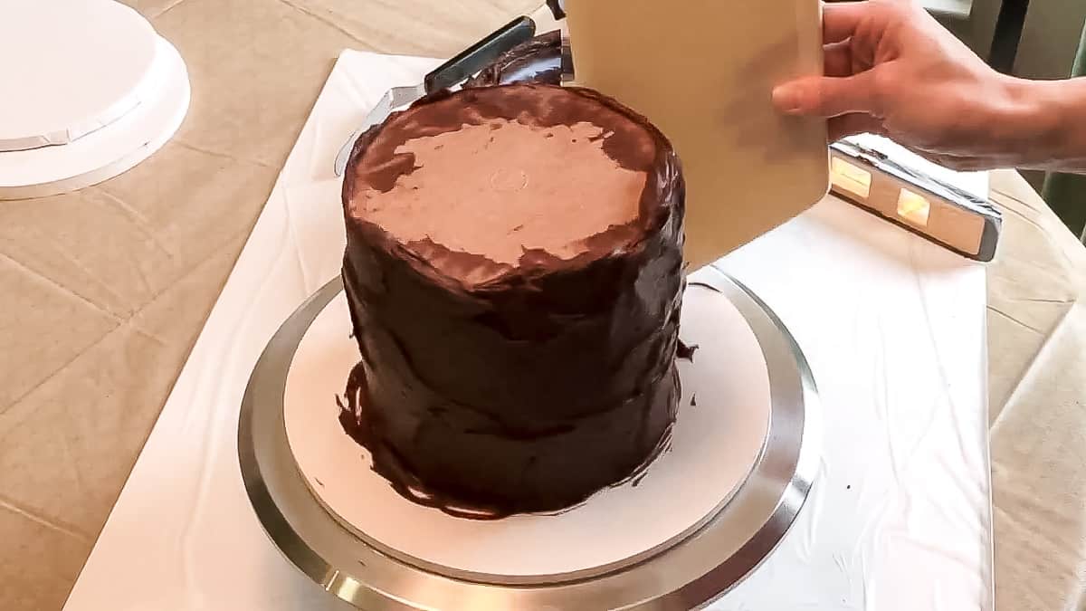 Using a smoother to smooth ganache on a cake.