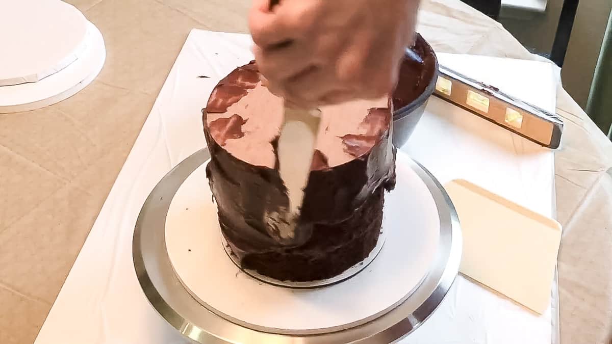 Adding ganache to cake with spatula.