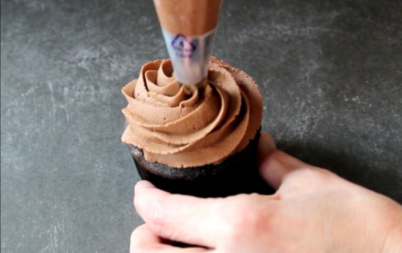 Piping chocolate buttercream onto chocolate cupcake
