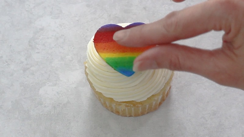 attaching rainbow buttercream heart shape to cupcake