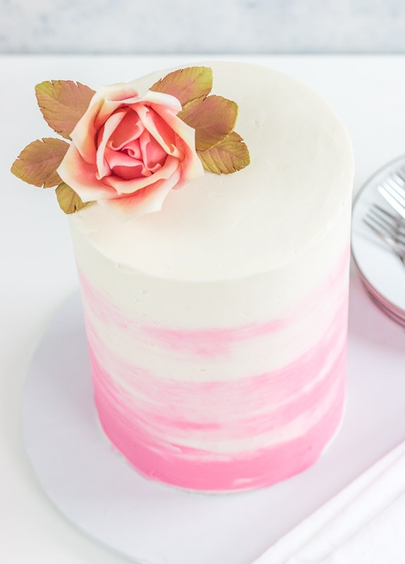 tall pink and white cake with pink rose on top