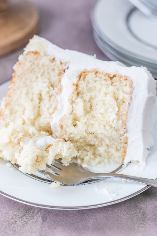 Slice of moist white cake on a white plate with a fork