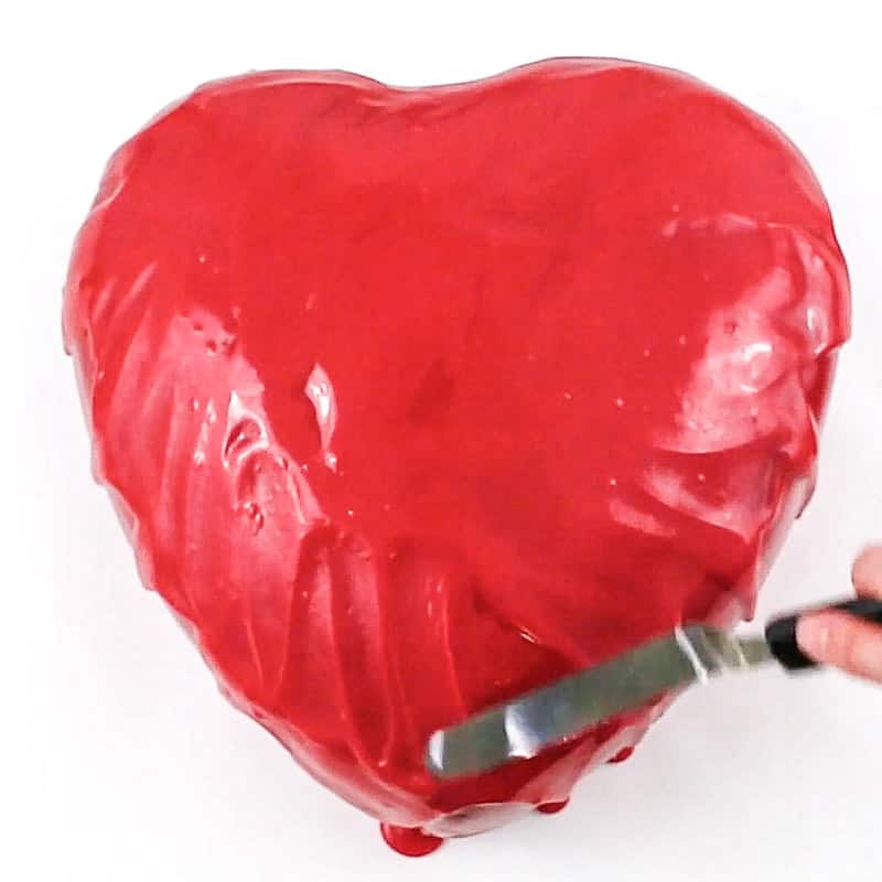 smoothing red ganache on heart cake
