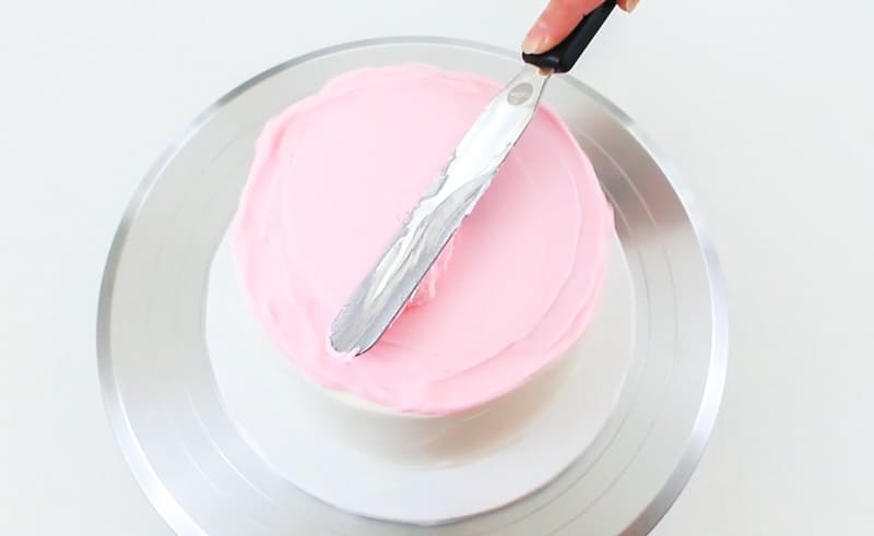smoothing pink buttercream on the top of the cake