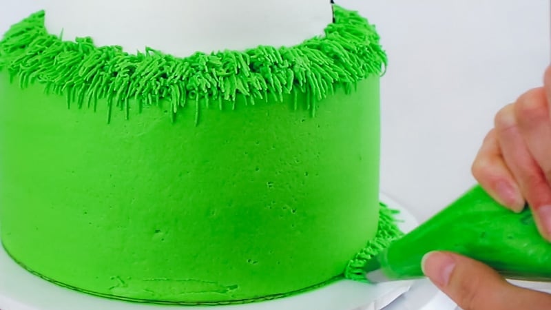 piping buttercream grass along bottom of cake