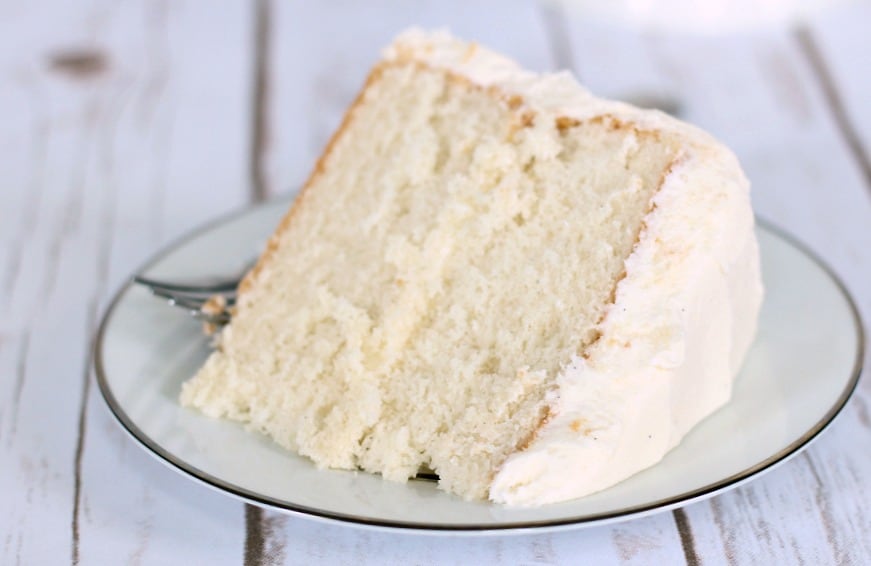 Large slice of white cake on a white plate and wood table.