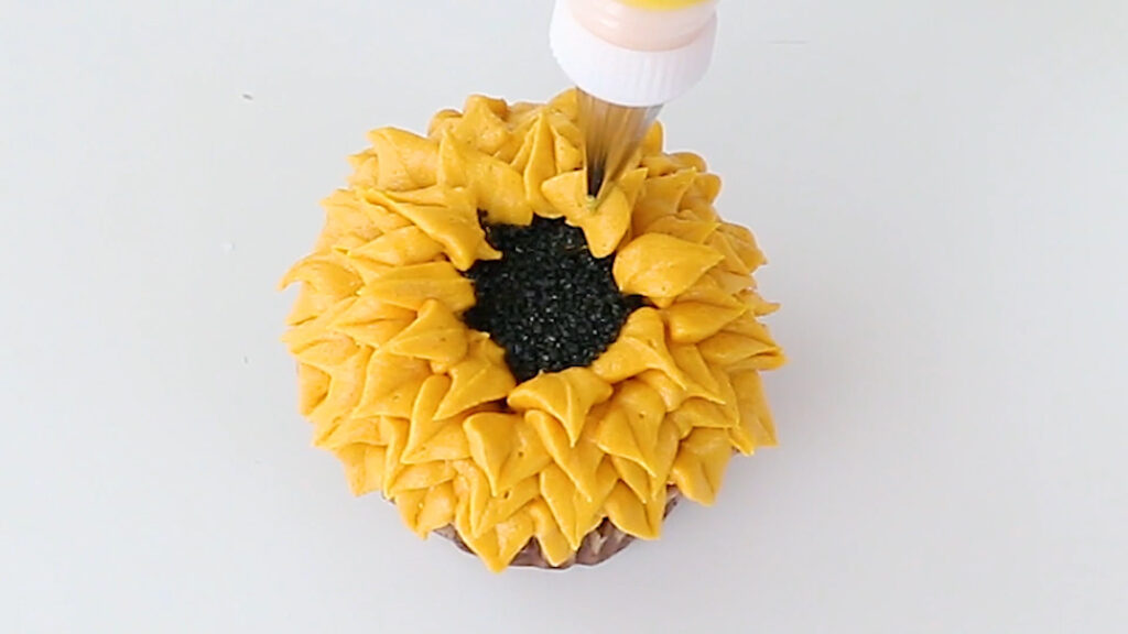 Finishing piping on yellow daisy cupcake.