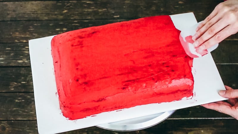 Smoothing red buttercream over rectangle cake.