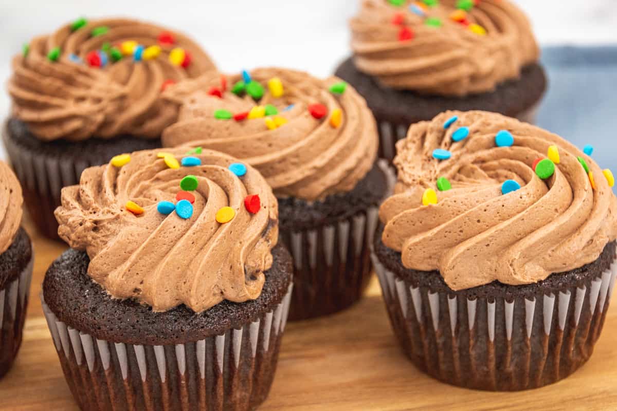 cupcakes with chocolate icing and sprinkles on a wooden board
