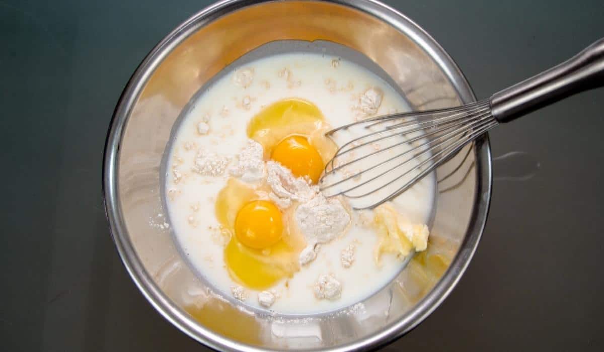 Bowl with eggs flour and milk with a whisk.