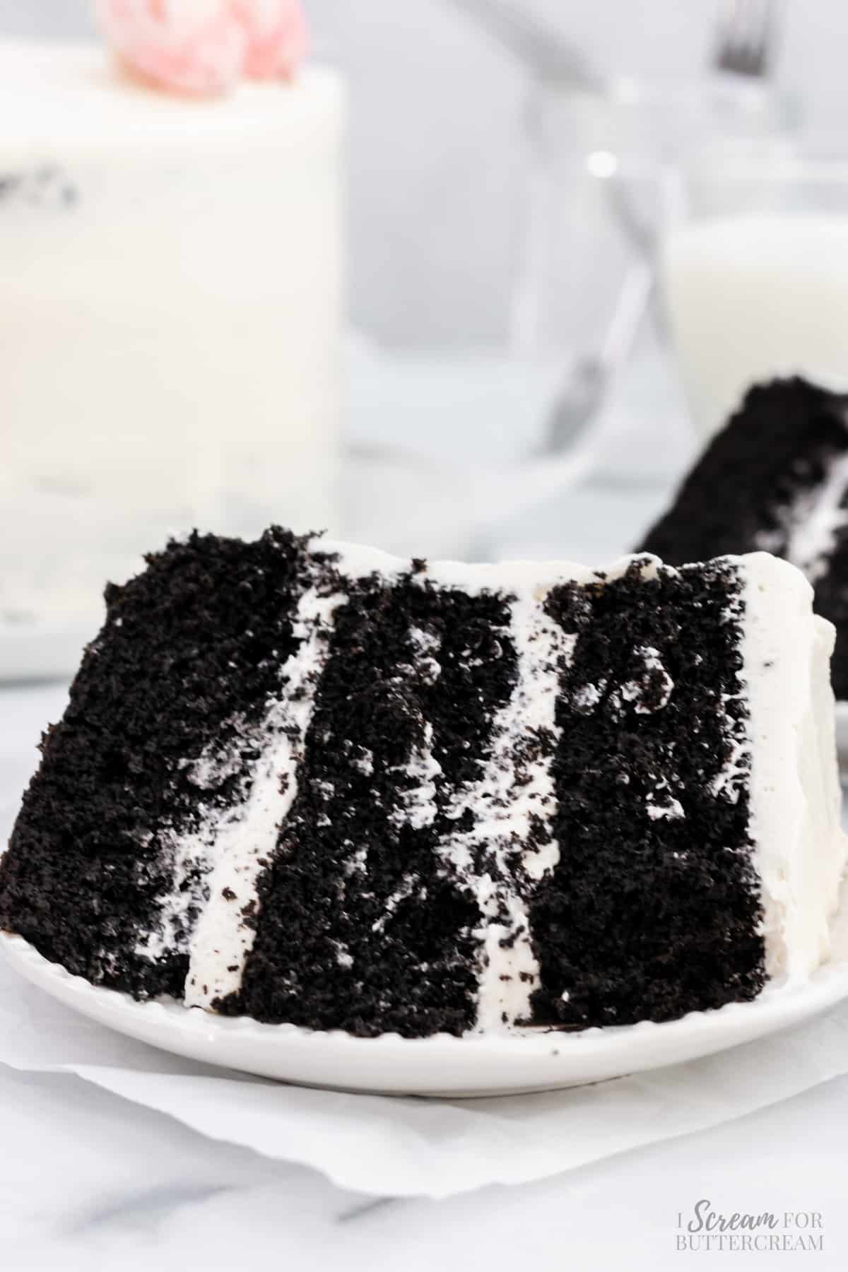 Close up of black cake with white icing on a white plate.