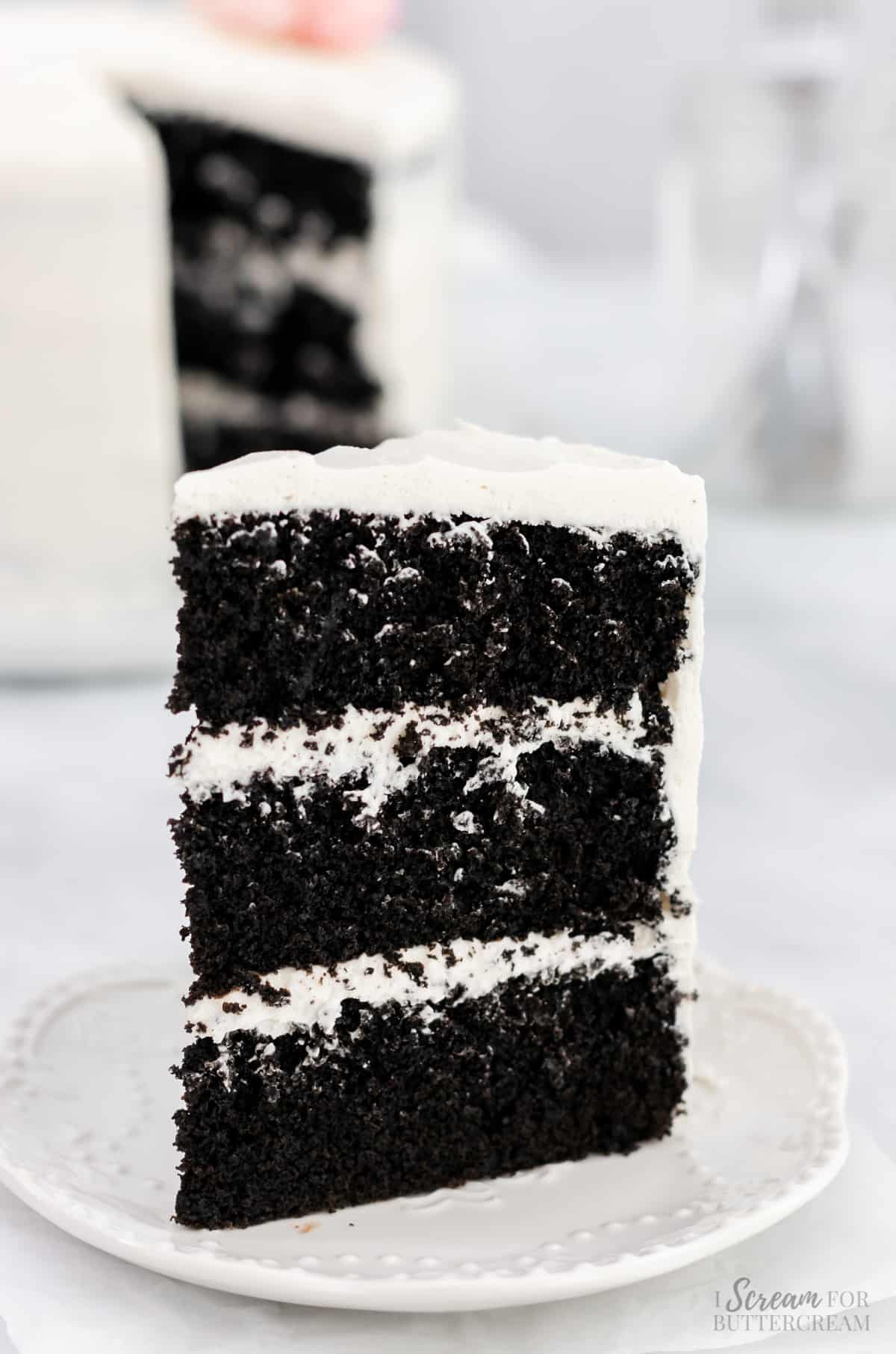 Three layer chocolate cake with white icing on a plate.