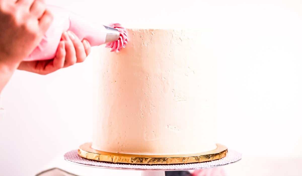 Hand piping buttercream on the side of a cake.