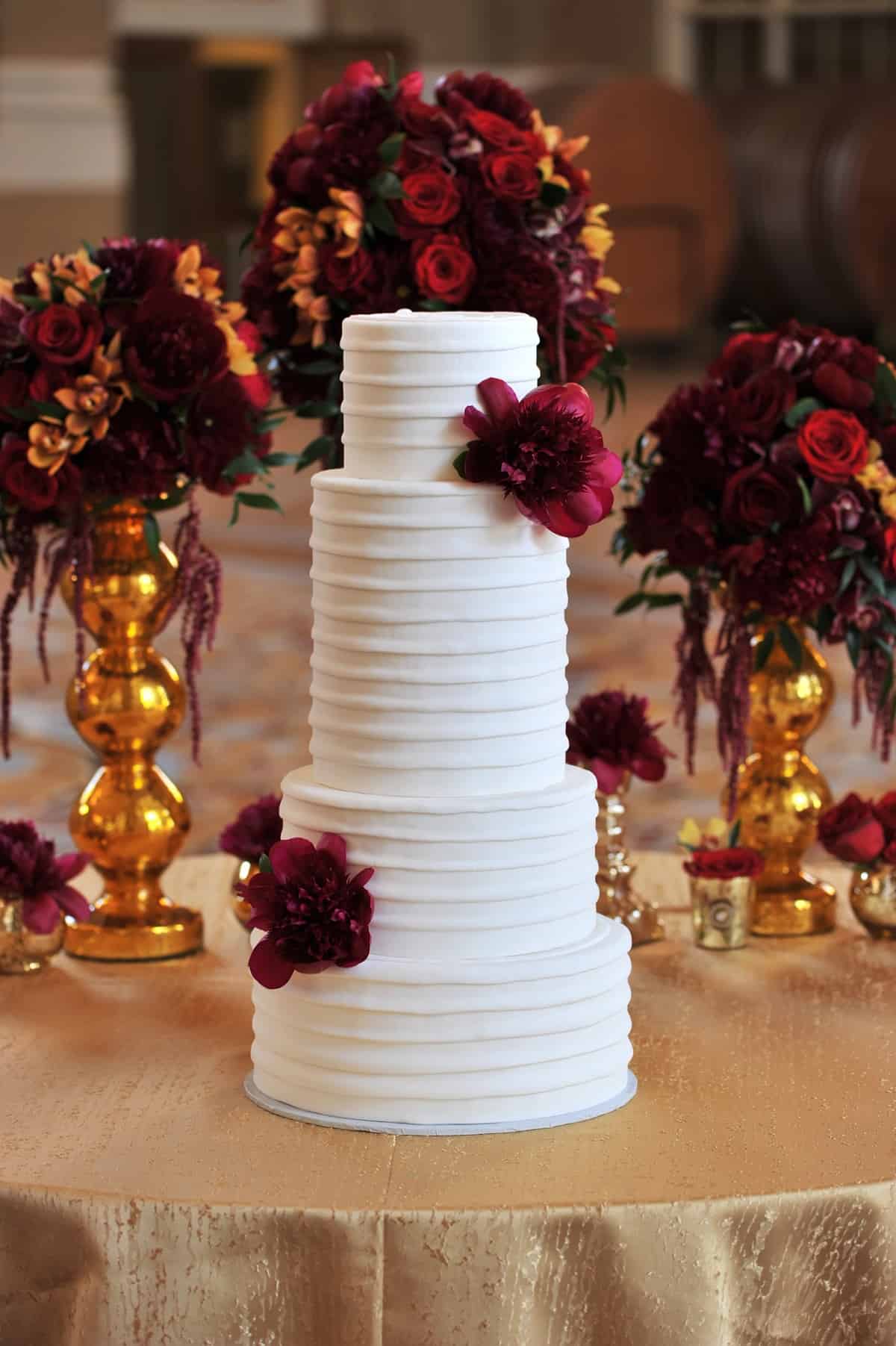Four tiered white wedding cake with red flowers.