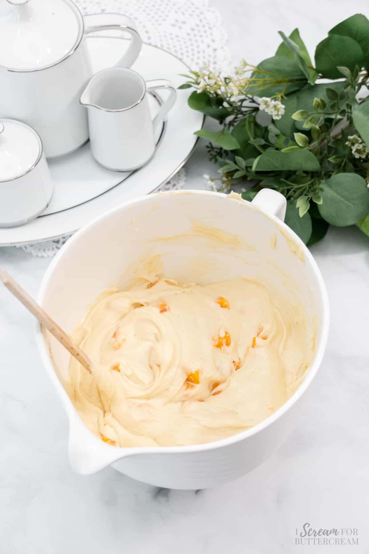 Peach cake batter in a mixing bowl with a spoon.