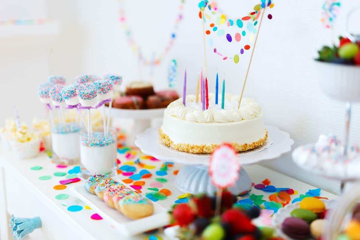 White cake with colorful candles and dessert table.