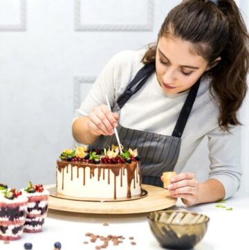 Lady decorating a cake on a table.