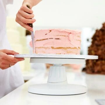Person decorating a cake with pink frosting.