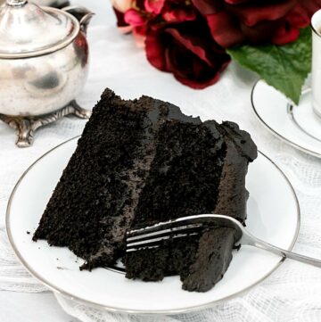 Square featured image of black cake on a white plate with a fork.