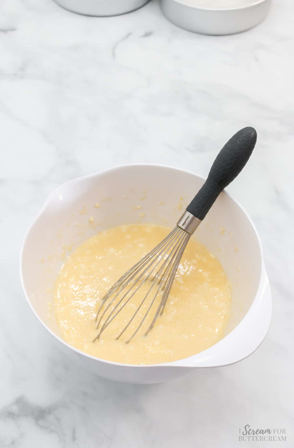 Liquid cake batter in a white bowl with a whisk.