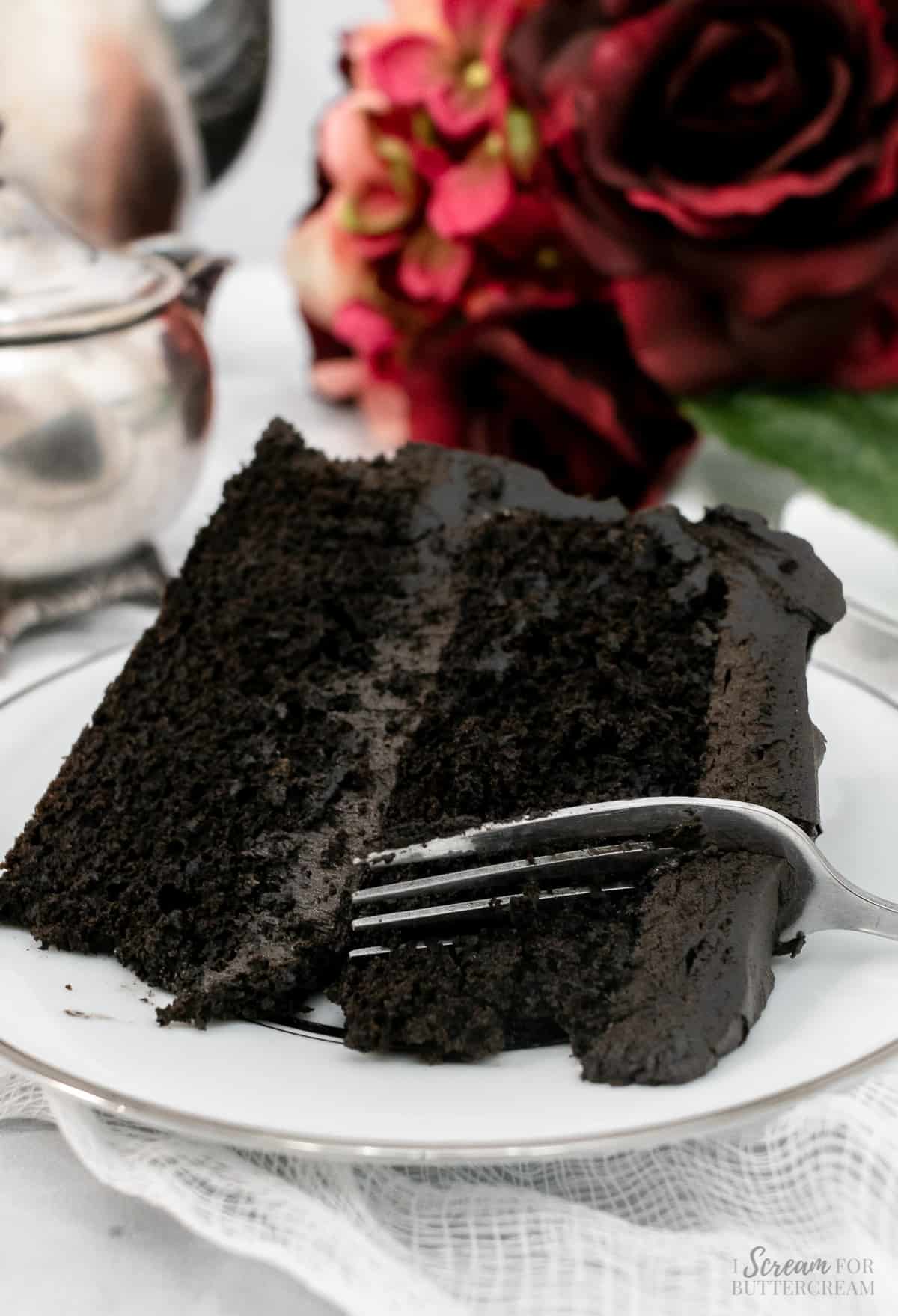 Slice of layer cake made with dark chocolate with a fork on a white plate.