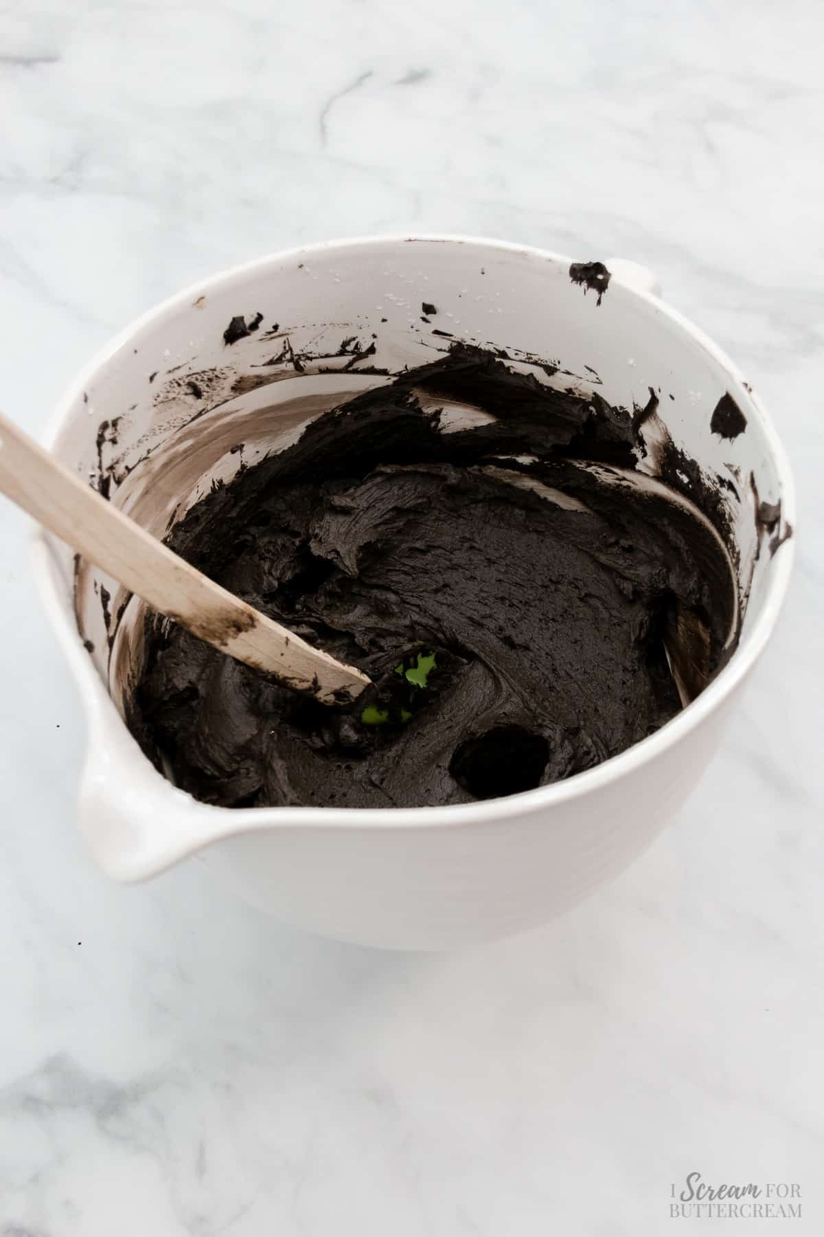 Black frosting in a white bowl with a spatula.