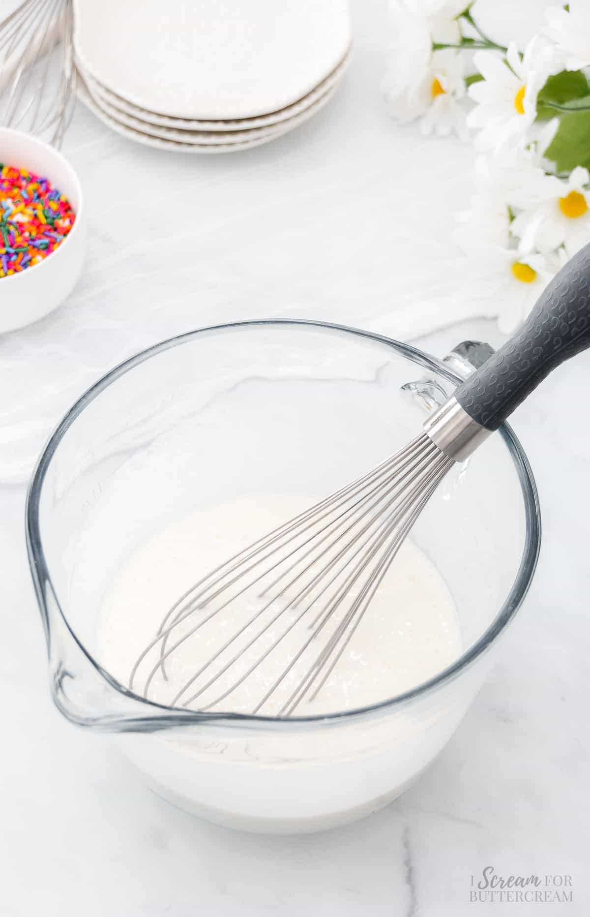 Liquid cake batter ingredients in a glass bowl with a whisk.