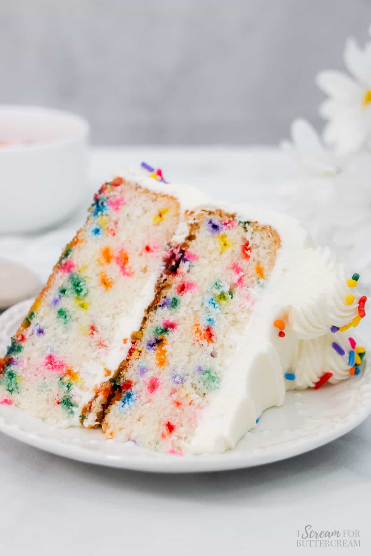 Slice of rainbow sprinkle cake on a white plate.