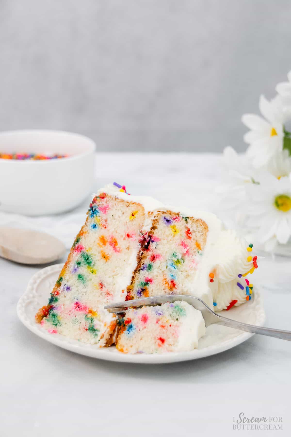 A slice of white cake with sprinkles and a fork on a white plate.