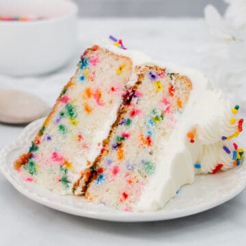 Slice of vanilla cake with sprinkles on a white plate.