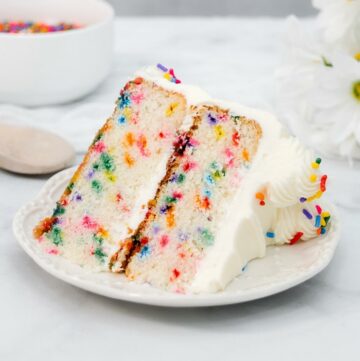 Large slice of rainbow sprinkle funfetti cake on a white plate.