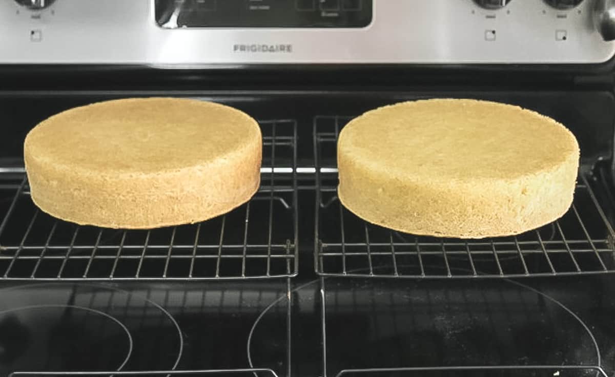 Cake layers cooling on wire racks on a stove.