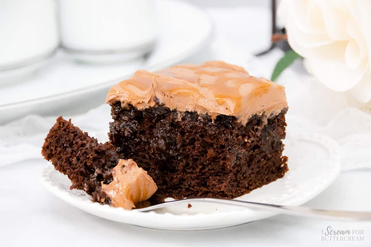 Large slice of caramel chocolate cake on a white plate with a fork.