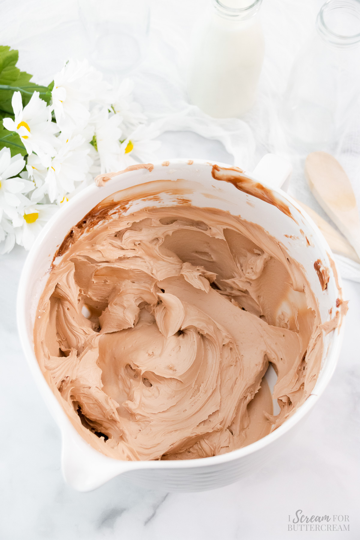 Milk chocolate icing mixed in a large white bowl.