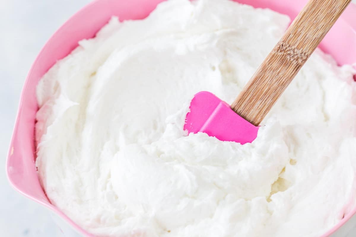 White buttercream in a pink bowl with a pink spatula.