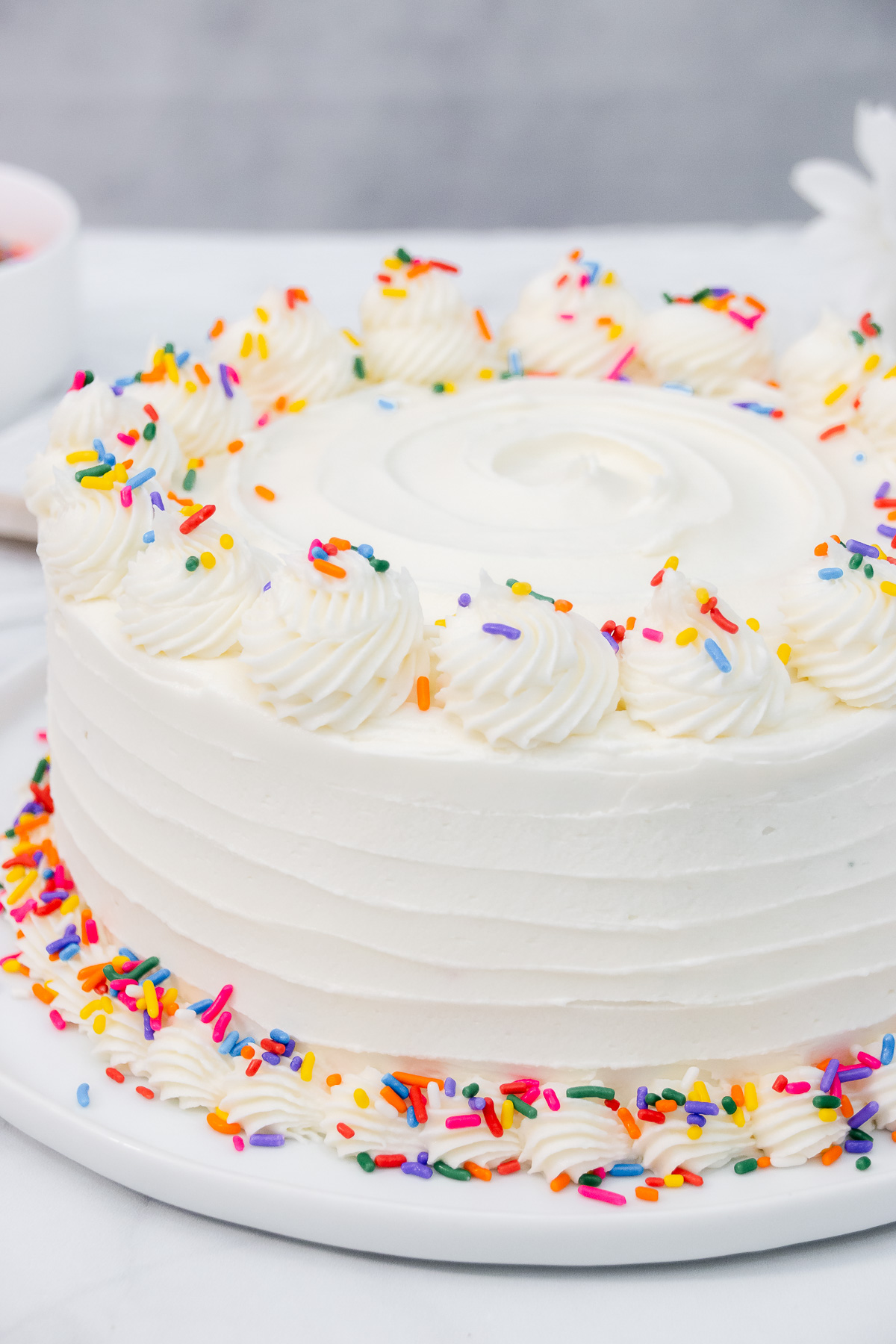 Vanilla buttercream cake with sprinkles on a white platter.