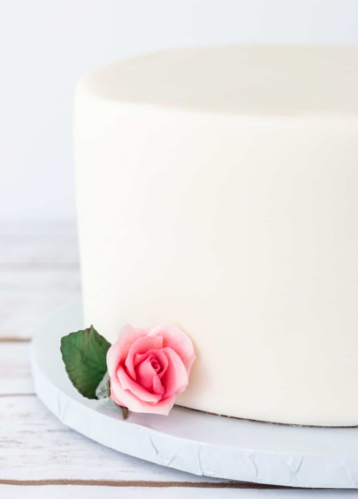 White fondant covered cake with a small pink rose.