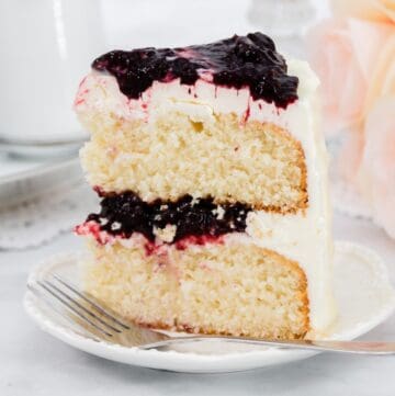 Close up of white layer cake with cherry frosting on a white plate with a fork.