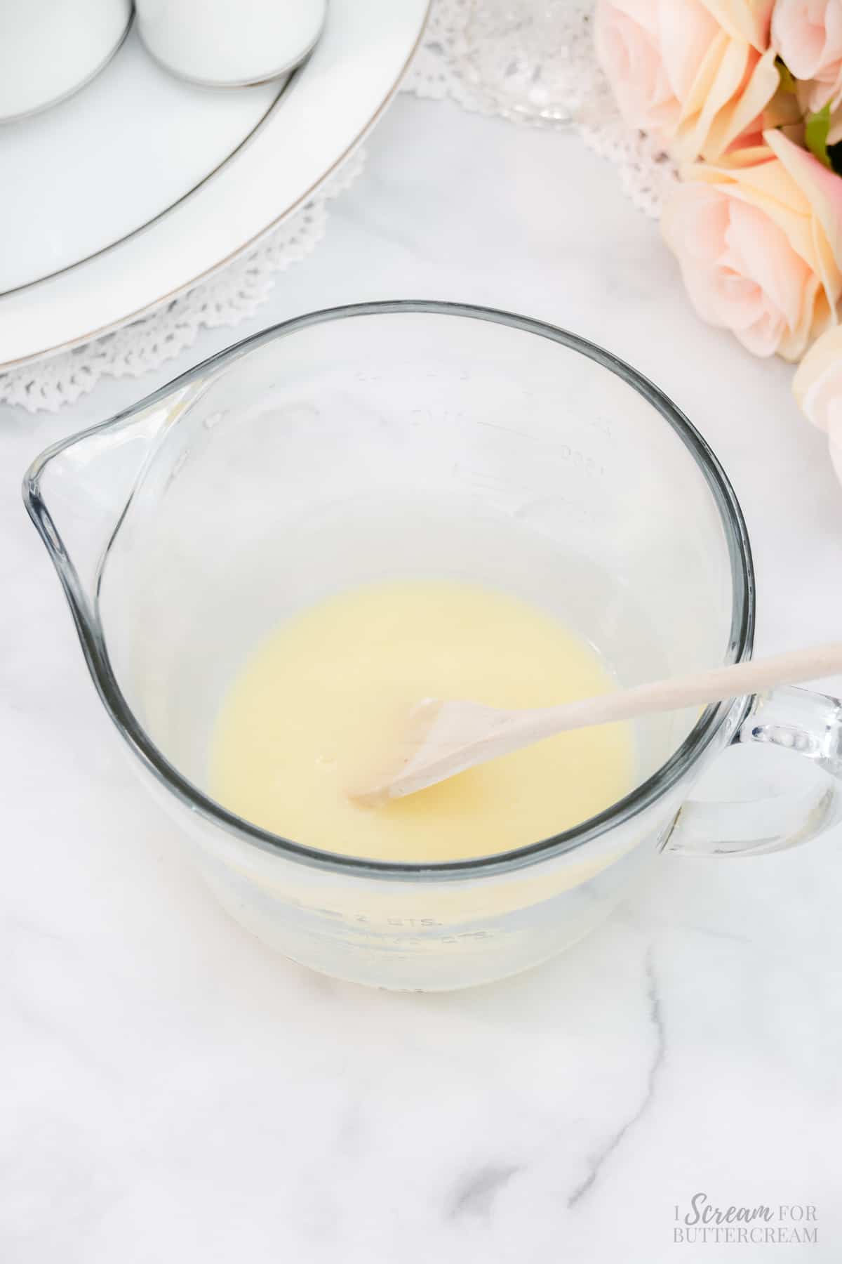 White chocolate ganache melted in a glass bowl with a spoon.