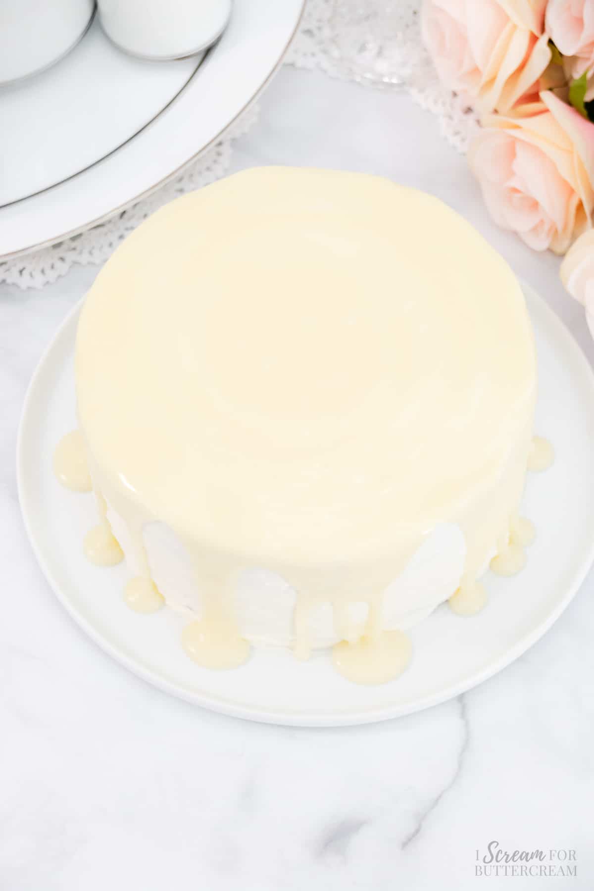 White chocolate ganache poured over the top of a frosted cake on a white platter.