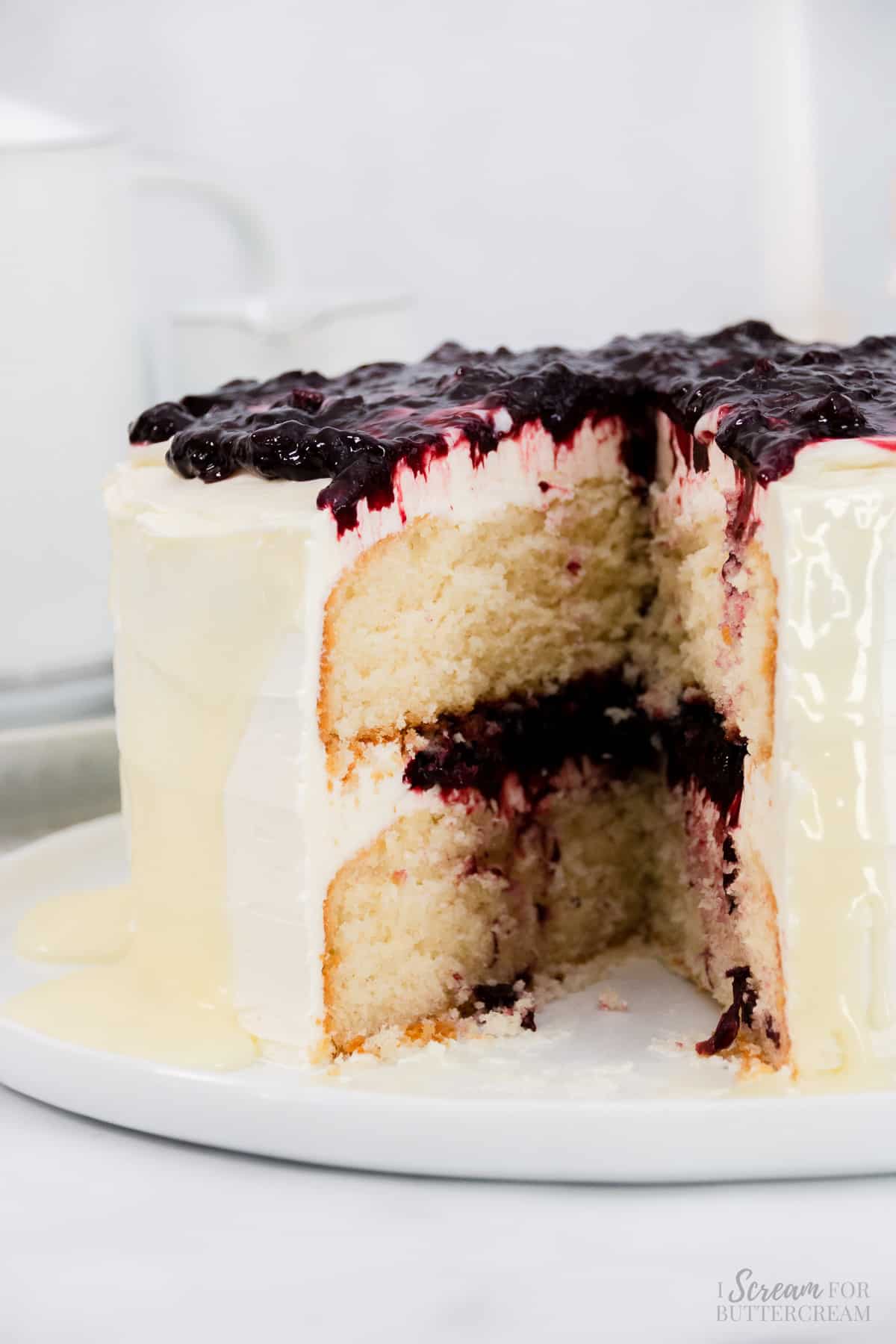Side view of white cake with cherry filling and white ganache drip on a white plate.