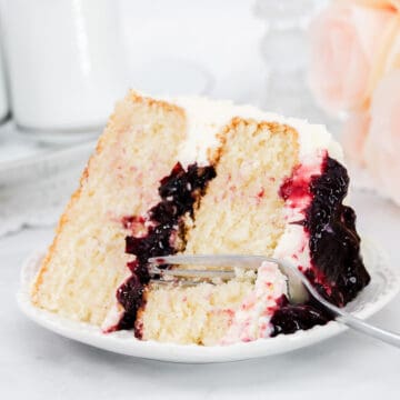 Featured image with large slice of white cake and cherry filling with a fork and a white plate.