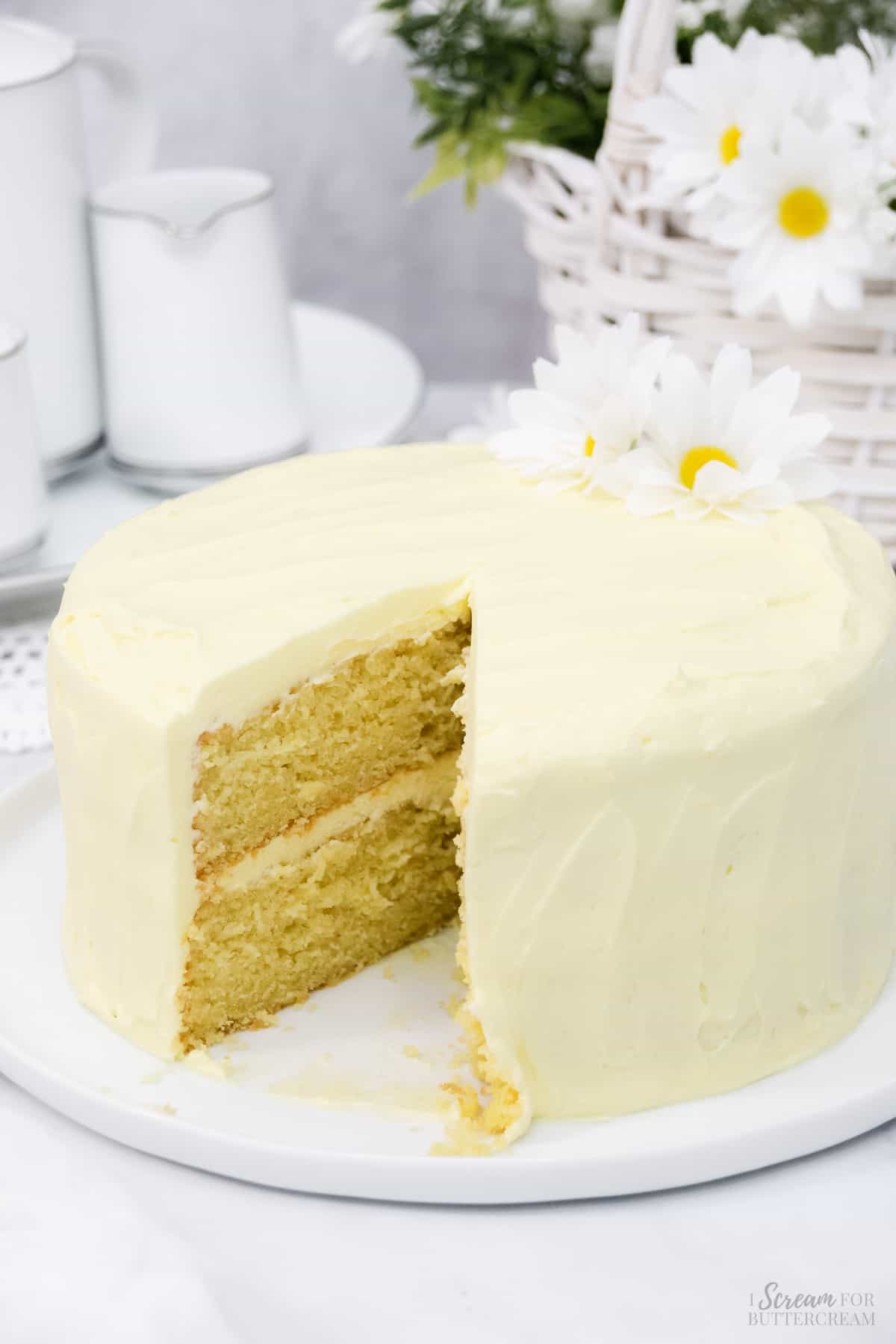 Decorated yellow cake with daisies on a white platter.