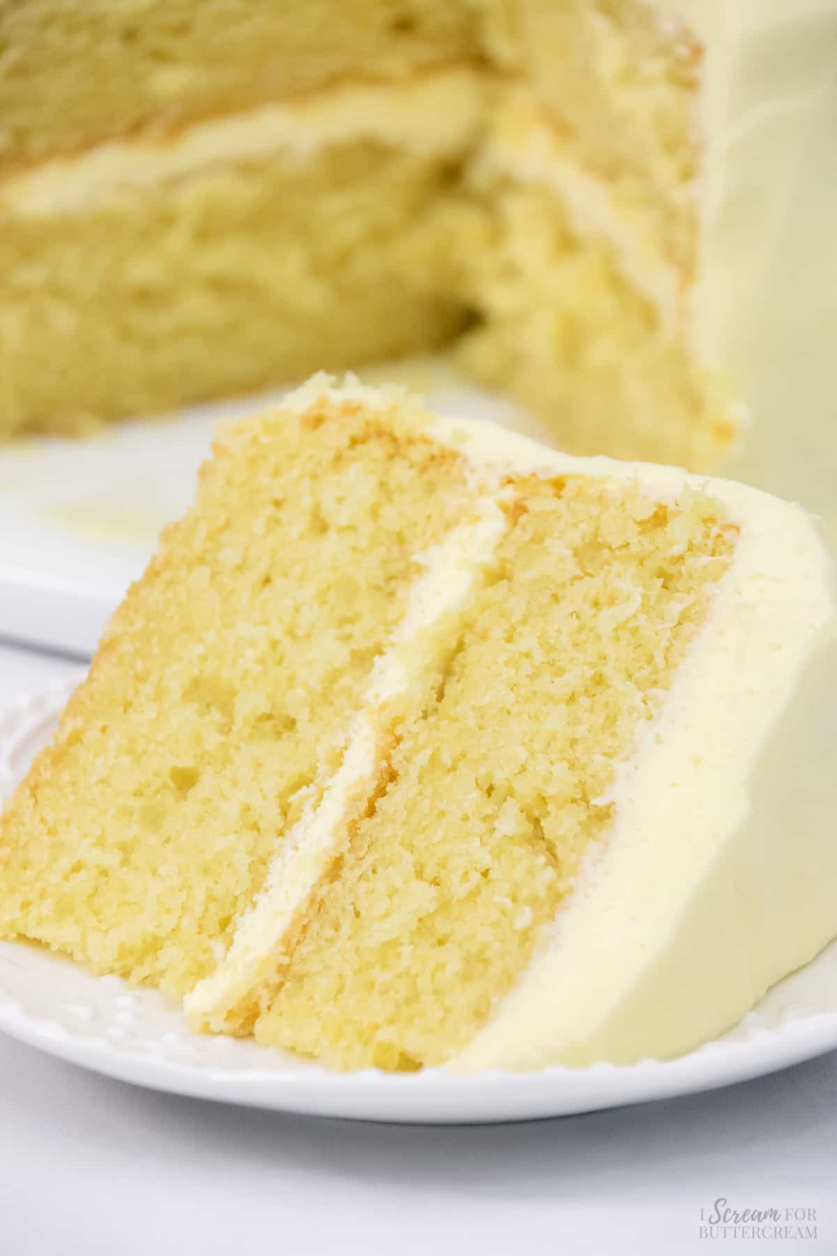 Tall image of lemon scratch cake with lemon frosting on a white plate.