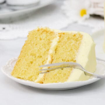 Yellow cake with lemon cream cheese frosting on a white plate with a fork.