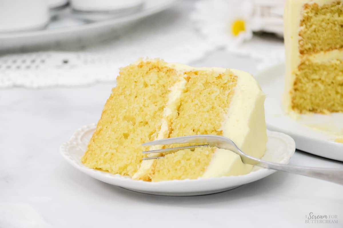 Yellow cake with lemon cream cheese frosting on a white plate with a fork.