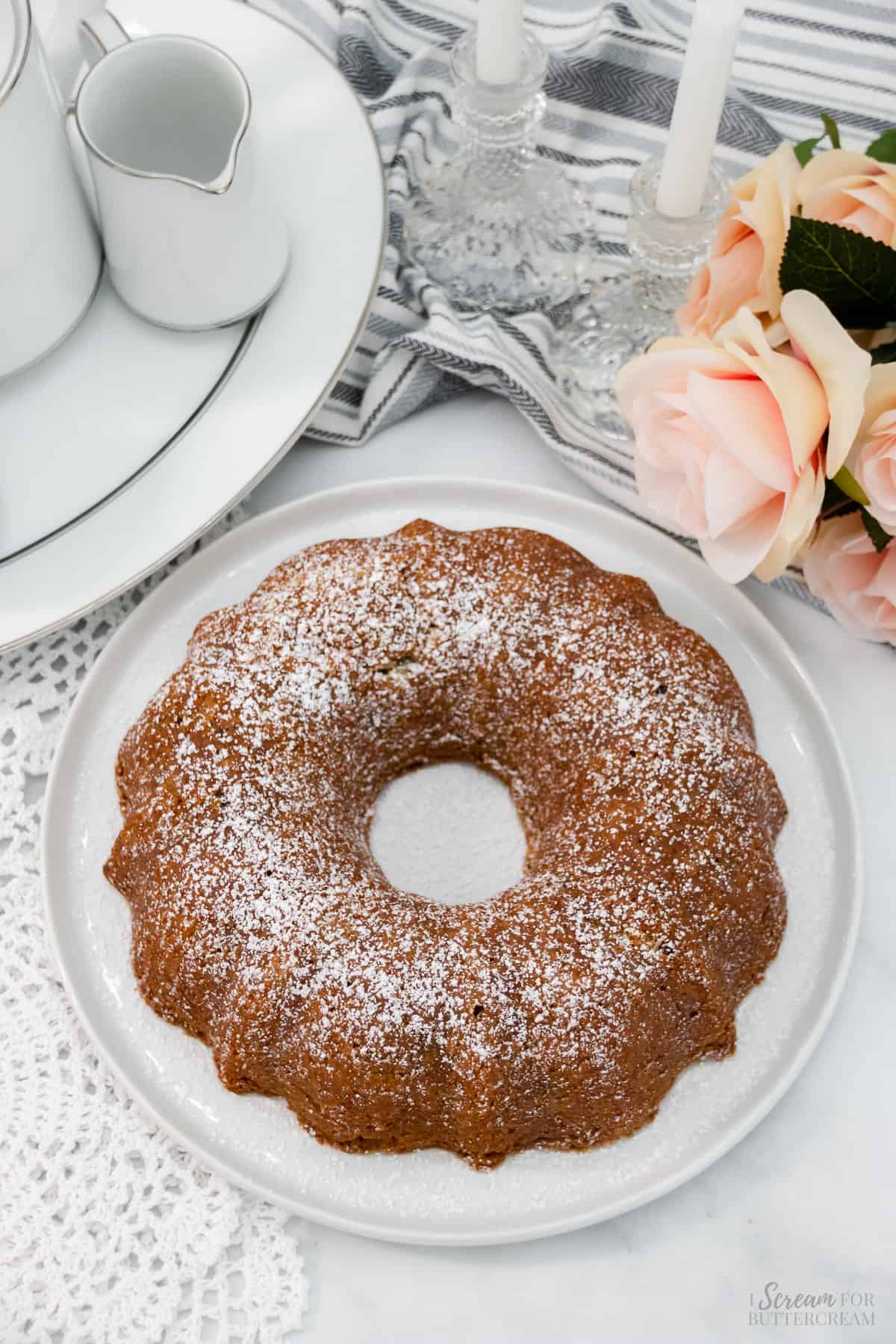 Top down view of bundt cake with powdered sugar over it with flowers and tea set and candles in the background.