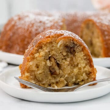 Large slice of bundt cake with coconut and nuts on a white plate with a fork.