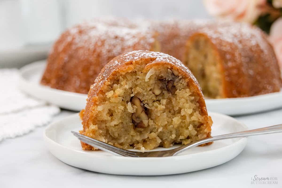 Large slice of bundt cake with coconut and nuts on a white plate with a fork.